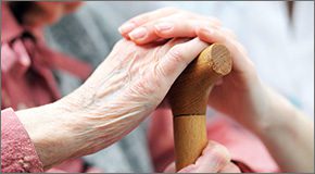 Close up of elder and younger female hands resting on top of a cane.