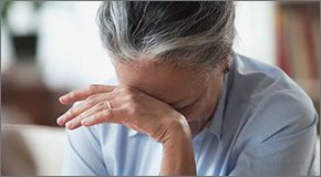 Elder woman with her head in her hand, looking distressed.