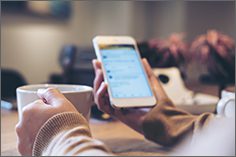 Woman with a cup of coffee in one hand and a cell phone in the other.